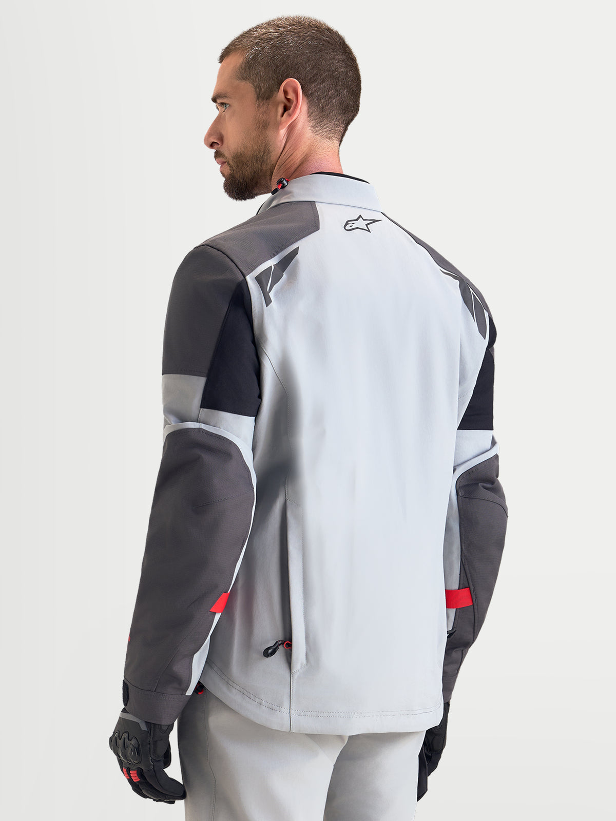 Alpinestars Arenis Gore-Tex, męska kurtka motocyklowa adventure w kolorze jasnoszarym, ciemnoszarym i czarnym, widok z tyłu na model prezentujący wodoodporną konstrukcję tekstylną i detale odblaskowe na ramionach