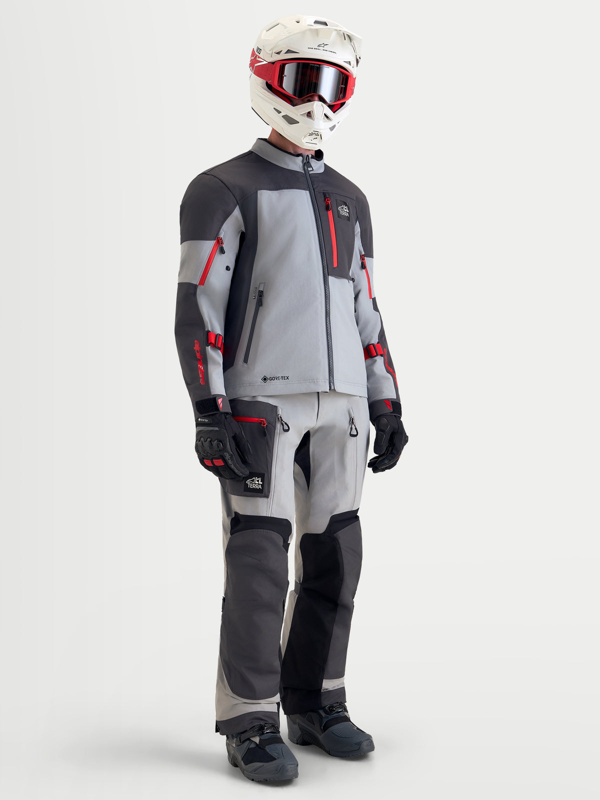 Alpinestars Arenis Gore-Tex kurtka motocyklowa adventure męska w kolorze średnioszarym, ciemnoszarym i czarnym z czerwonymi akcentami, pełny zestaw ze spodniami, kaskiem i goglami na modelu