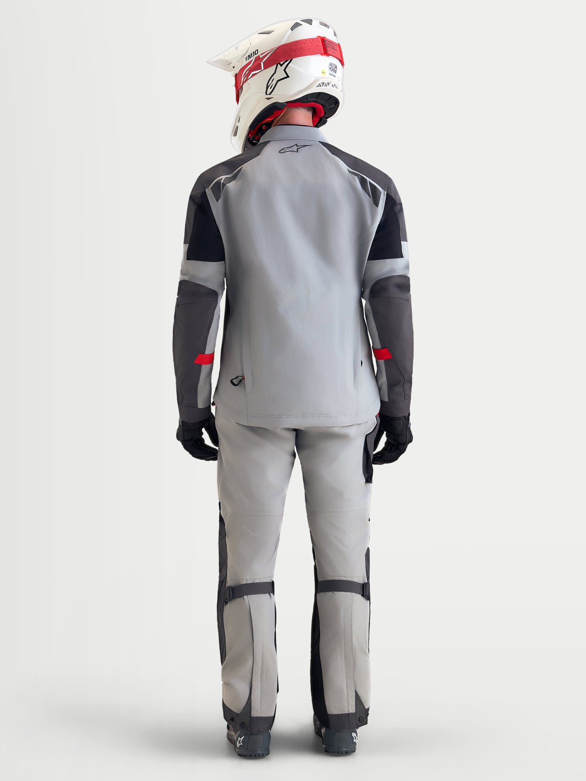 Alpinestars Arenis Gore-Tex kurtka motocyklowa męska adventure w kolorze jasnoszarym, ciemnoszarym i czarnym, widok z tyłu na model w wodoodpornej tekstylnej kurtce z kaskiem i wyposażeniem
