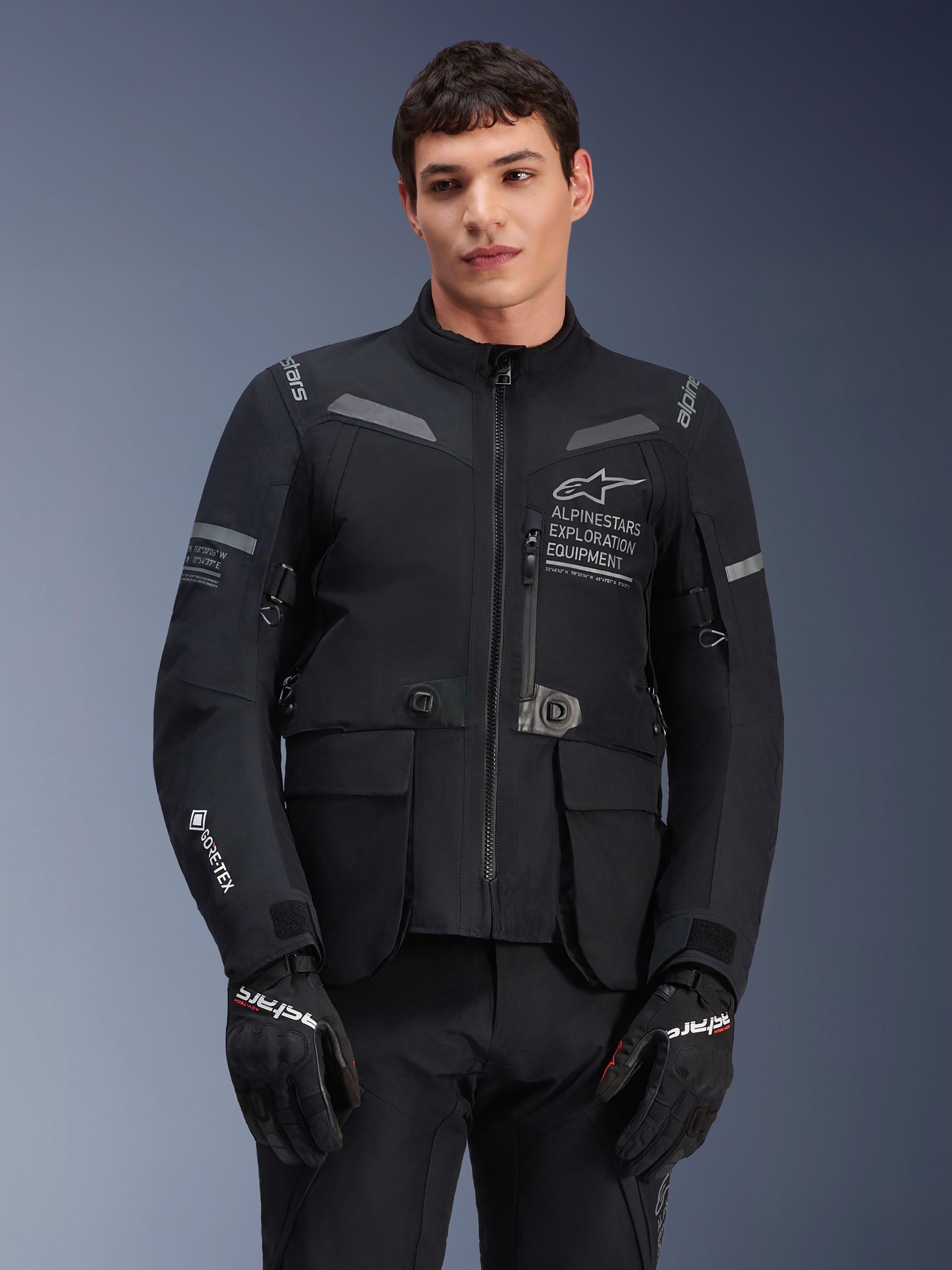 Alpinestars ST-7 2L GORE-TEX Jacket, motocyklowa kurtka turystyczna, czarna i ciemnoszara, z logo Alpinestars Exploration Equipment na piersi, dużymi wodoodpornymi kieszeniami cargo, logo GORE-TEX na rękawie, wytrzymała konstrukcja z odblaskowymi akcentami