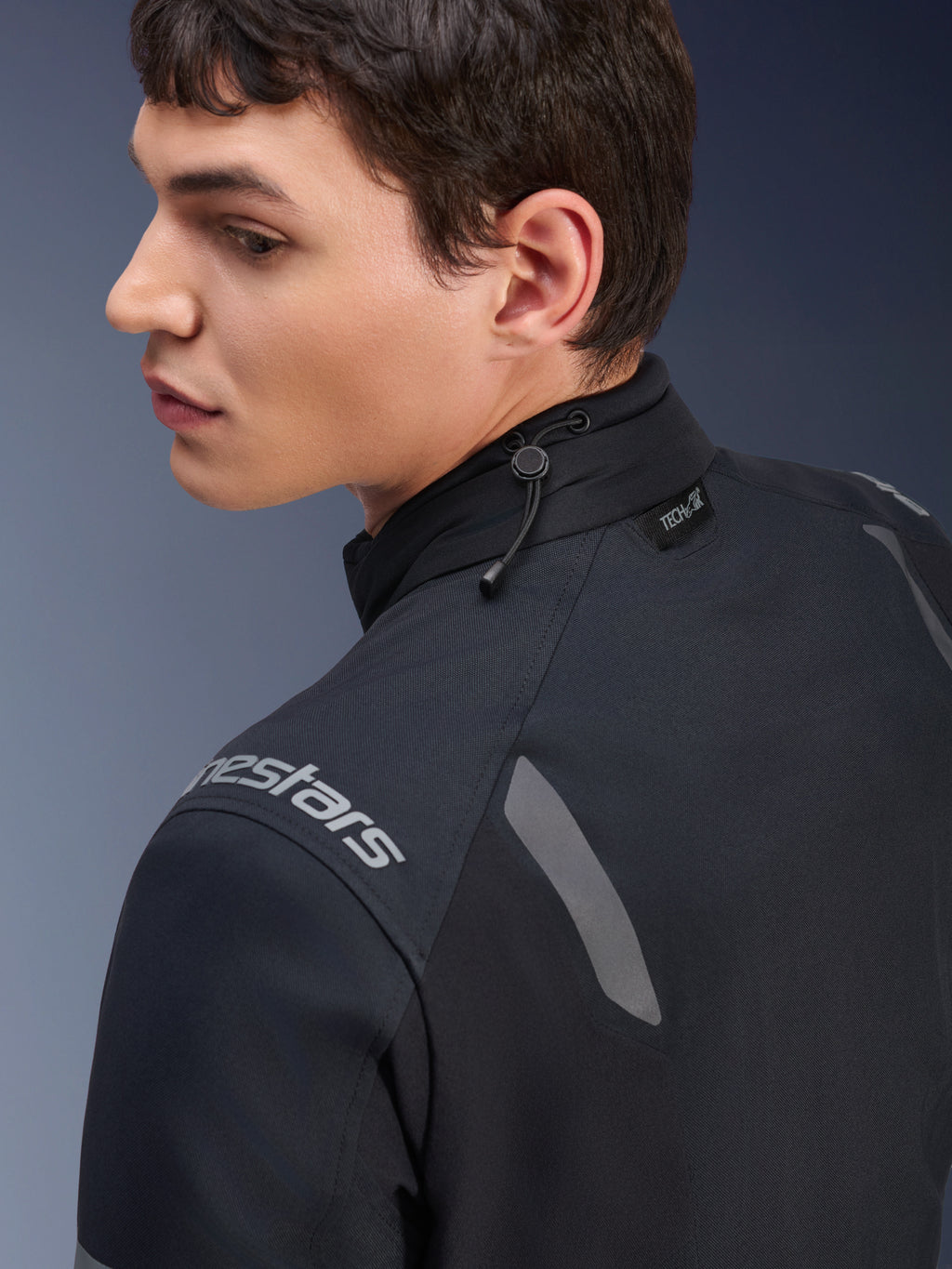 Kurtka Alpinestars ST-7 2L GORE-TEX, czarno-ciemnoszara kurtka motocyklowa, zbliżenie na kołnierz pokazujące regulację ściągaczem i etykietę Tech-Air, szare odblaskowe akcenty oraz logo marki na ramieniu