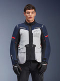 Kurtka Alpinestars ST-7 2L GORE-TEX, motocyklowa kurtka turystyczna adventure, lodowoszara i ciemnoniebieska z czerwonymi akcentami, wodoodporna i oddychająca, prezentowana na modelu w czarnych rękawicach, z logo Alpinestars Exploration Equipment na klatce piersiowej