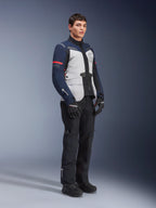 Kurtka Alpinestars ST-7 2L GORE-TEX w kolorystyce Ice Gray, Dark Blue i czarnej z czerwonymi akcentami, noszona przez modela z czarnymi spodniami motocyklowymi i rękawicami, profesjonalna odzież motocyklowa adventure touring