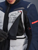 Kurtka Alpinestars ST-7 2L GORE-TEX, kurtka adventure touring, lodowy szary, granatowy i czarny, szczegółowy widok rozpiętego panelu wentylacyjnego na klatce piersiowej odsłaniającego czarną siatkę, logo Alpinestars Exploration Equipment i czerwone uchwyty zamków