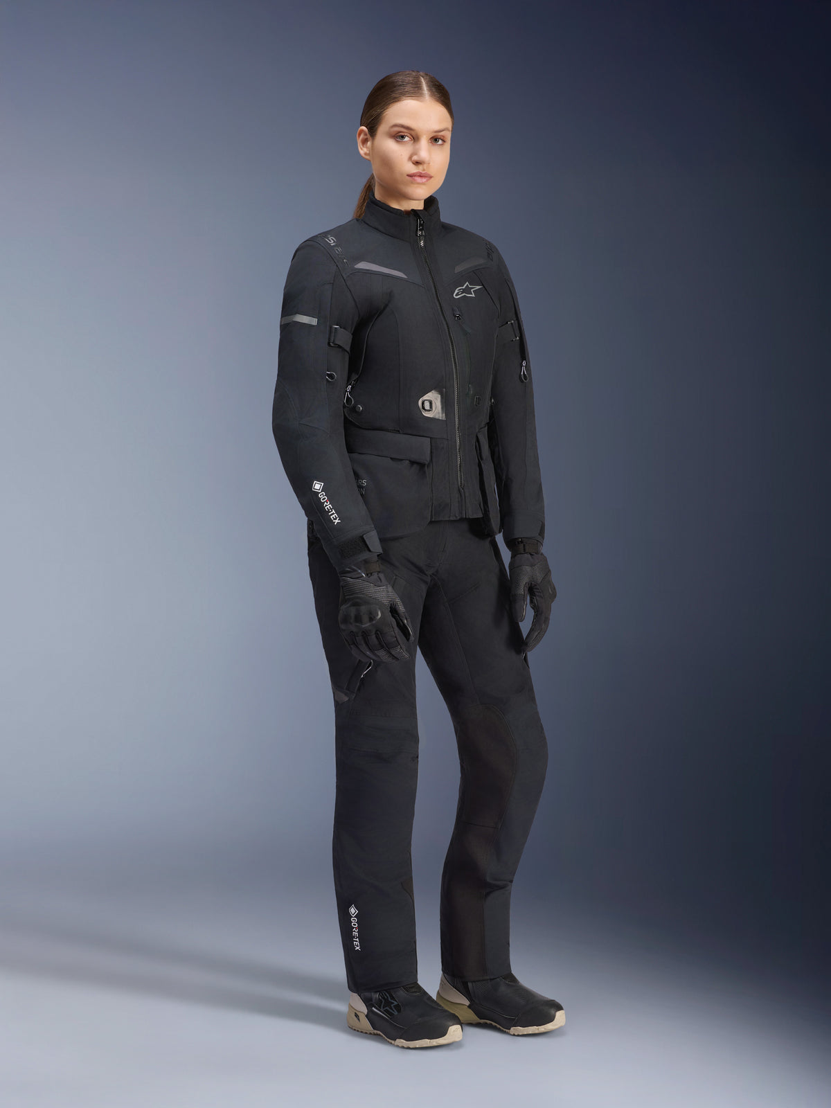 Damska kurtka Alpinestars Stella ST-7 2L GORE-TEX, czarna, noszona z pasującymi spodniami motocyklowymi i rękawicami, zestaw adventure road-touring z laminowanym logo GORE-TEX na rękawie i dopasowanym damskim krojem.