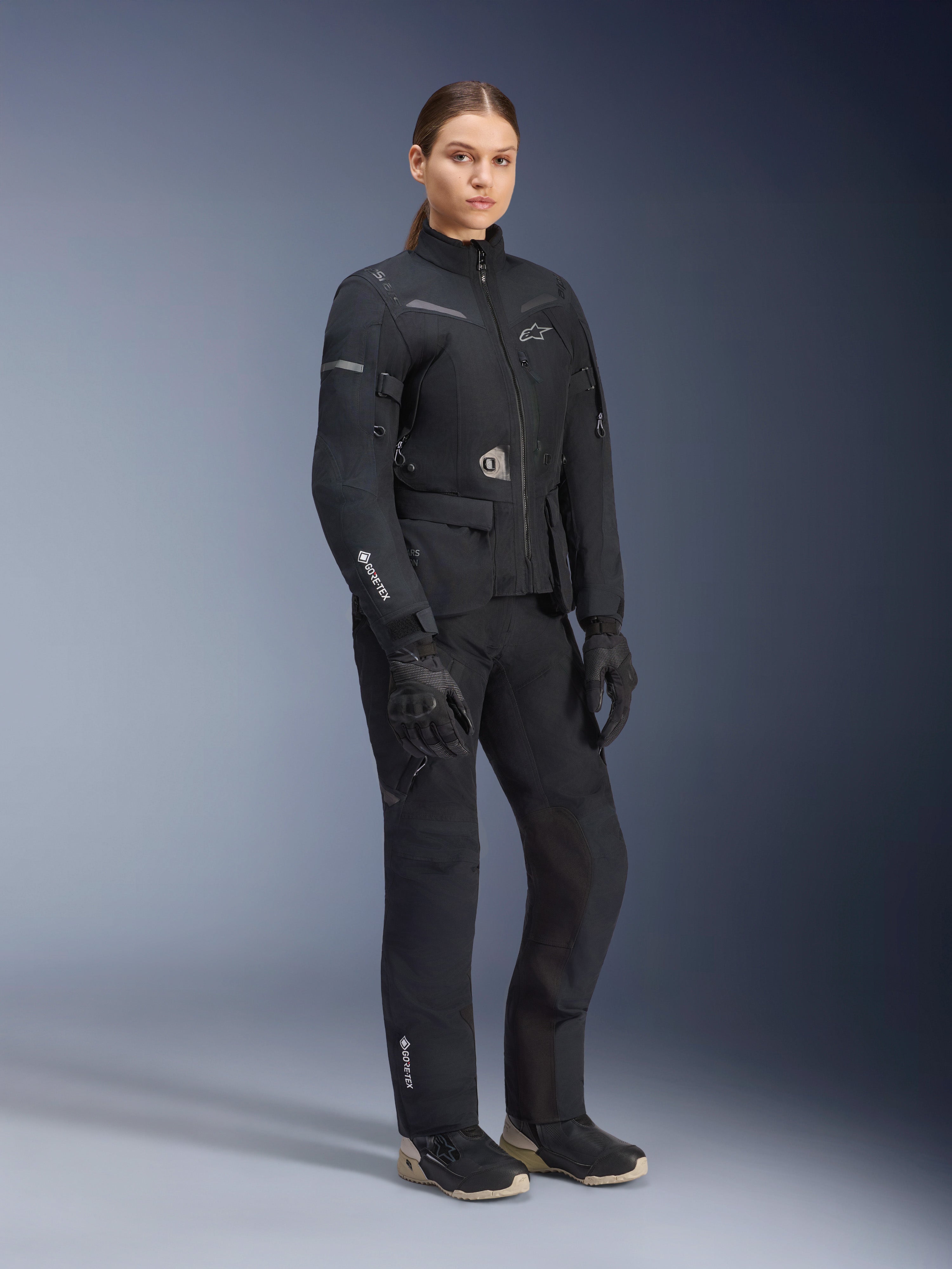 Damska kurtka Alpinestars Stella ST-7 2L GORE-TEX, czarna, noszona z pasującymi spodniami motocyklowymi i rękawicami, zestaw adventure road-touring z laminowanym logo GORE-TEX na rękawie i dopasowanym damskim krojem.