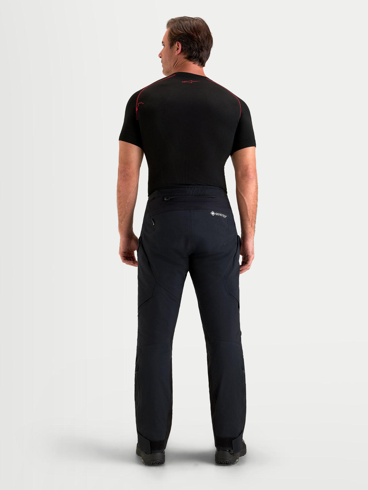 Alpinestars St-7 V2 2L Gore-Tex Spodnie motocyklowe adventure krótkie, męskie, czarne, widok z tyłu na model w wodoodpornym stroju tekstylnym z pasującą ciemną górą