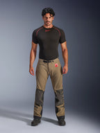 Model w spodniach Alpinestars Nazca 3L GORE-TEX PRO w kolorze orzechowego brązu i czerni, techniczna odzież motocyklowa typu adventure ze wzmocnieniami kolan Superfabric i magnetyczną klamrą w pasie, w połączeniu z czarną koszulką termoaktywną Alpinestars, widok z przodu w studio.