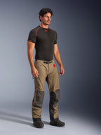 Alpinestars Nazca 3L GORE-TEX PRO Pants w kolorze Walnut Black, przygodowe spodnie motocyklowe z czarnymi wzmocnieniami Superfabric na kolanach, prezentowane przez modela w czarnej warstwie kompresyjnej, wyposażone w pasek z klamrą magnetyczną i czerwony branding All Terra.