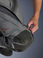 Spodnie Alpinestars Nazca 3L GORE-TEX PRO, motocyklowe spodnie adventure, ciemnoszare i czarne, zbliżenie na dłoń otwierającą zapinany na zamek wlot wentylacyjny na udzie, wzmocnienia kolan z teksturowanego materiału Superfabric, czerwone logo gwiazdy Alpinestars, techniczna konstrukcja tekstylna zapewniająca ochronę w każdych warunkach pogodowych