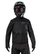 Kurtka Alpinestars Pro-Dura, czarna kurtka motocyklowa off-road, widok z przodu, noszona przez motocyklistę w czarnym kasku i goglach, czerwone logo Alpinestars, zapinane na zamek kieszenie na klatce piersiowej, wytrzymała konstrukcja tekstylna do jazdy enduro.
