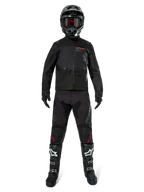 Kurtka Alpinestars Pro-Dura, czarna kurtka enduro off-road, pokazana na modelu z pełnym zestawem odzieży, w tym czarny kask z czerwonymi goglami, czarne spodnie z czerwonymi akcentami, czarno-białe buty i czarne rękawice, wytrzymała konstrukcja inspirowana rajdami do jazdy terenowej
