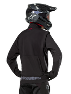 Kurtka Alpinestars Lite-Dura Softshell, czarna, widok z tyłu na motocykliście, szary napis Alpinestars na dolnym brzegu i małe czerwone logo na kołnierzu, zestaw z czarnym kaskiem motocrossowym, do jazdy enduro i off-road
