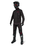 Kurtka Alpinestars Lite-Dura Softshell, czarna, zaprezentowana na manekinie w kompletnym zestawie off-road z czarnymi spodniami, czarno-białymi butami i czarnym kaskiem z czerwonymi goglami, profesjonalna odzież motocrossowa i enduro.