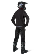Zawodnik enduro widziany od tyłu w czarnej kurtce Alpinestars Lite-Dura Softshell, zestawiony z czarnymi technicznymi spodniami i butami motocyklowymi, z tylną kieszenią na zamek i logo Alpinestars na dolnym brzegu, kompletny strój off-road do motocrossu.