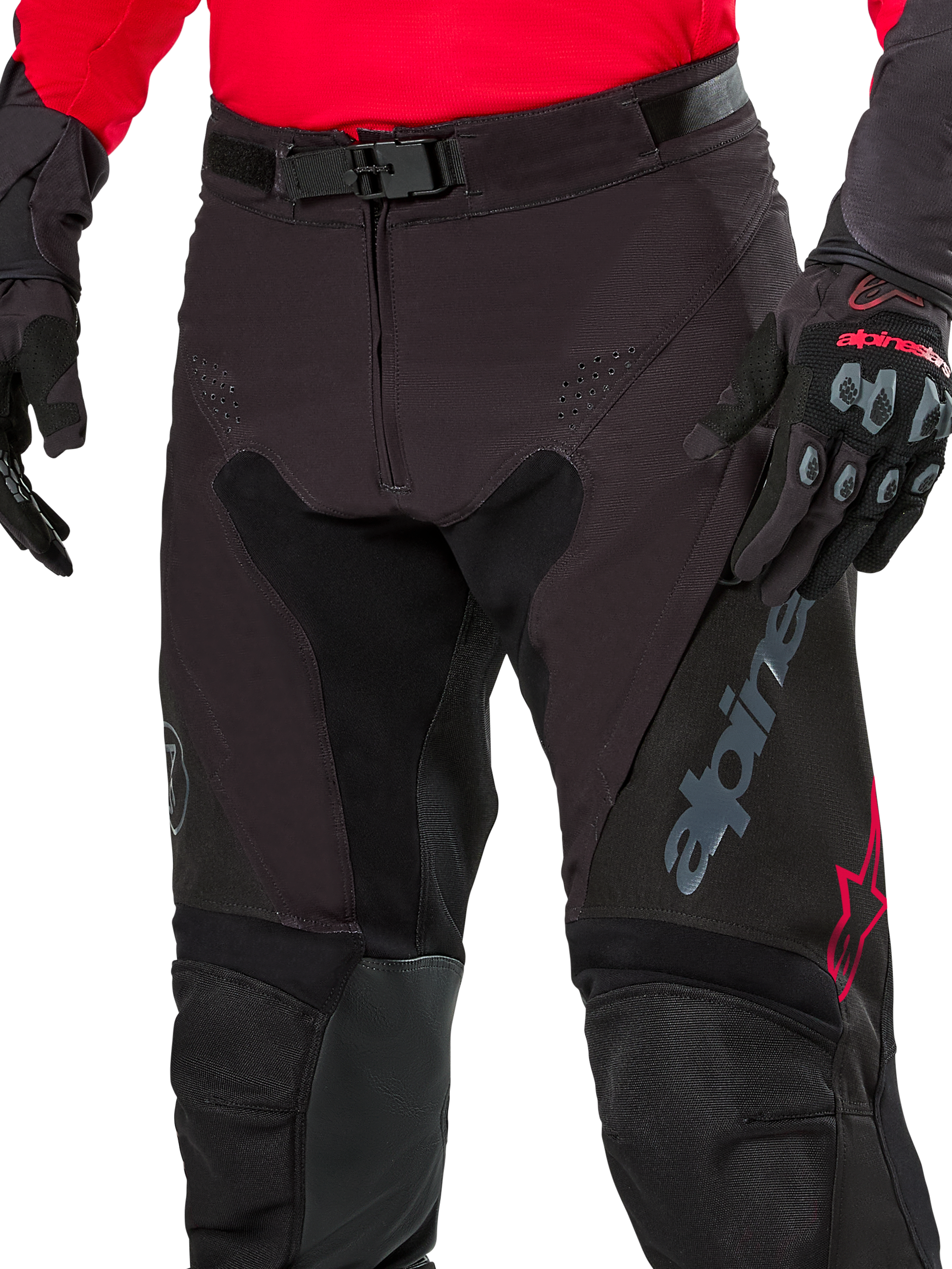 Close-up of Alpinestars Pro-Dura Pants, Enduro Pants, Black Magnet White with red accents, featuring a secure magnetic buckle closure and zip fly, worn with matching red jersey and black gloves, durable ripstop construction for off-road riding