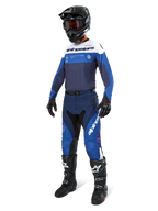 Motocyklista motocrossowy ubrany w spodnie Alpinestars Pro-Dura w kolorach granatowym, jasnoniebieskim i białym, w zestawie z pasującą bluzą z długim rękawem, czarnym kaskiem z czerwonymi goglami, czarnymi rękawicami i czarno-białymi butami, skoordynowany strój do wyścigów enduro i off-road.