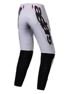 Alpinestars 2025 Supertech Maker Pants, spodnie motocrossowe, srebrne i czarne, widok z tyłu z dużym czarnym logo Alpinestars z boku, czarne panele w dolnej części nogawek i małe czerwone logo gwiazdy na pasku, zaprojektowane dla profesjonalnych osiągów w terenie