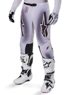Alpinestars Supertech Maker Pants 2025, spodnie motocrossowe, srebrno-czarne, z dużym logo gwiazdy i czerwonymi napisami, prezentowane z dopasowanymi białymi butami i rękawicami