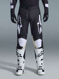 Alpinestars 2026 Racer Air Riway Pants, spodnie motocrossowe, czarno-białe, z wyraźnymi białymi logotypami Alpinestars na udach i panelach kolanowych, w zestawieniu z biało-czarnymi butami motocrossowymi i czarnymi rękawicami, sportowy krój race-fit do jazdy off-road