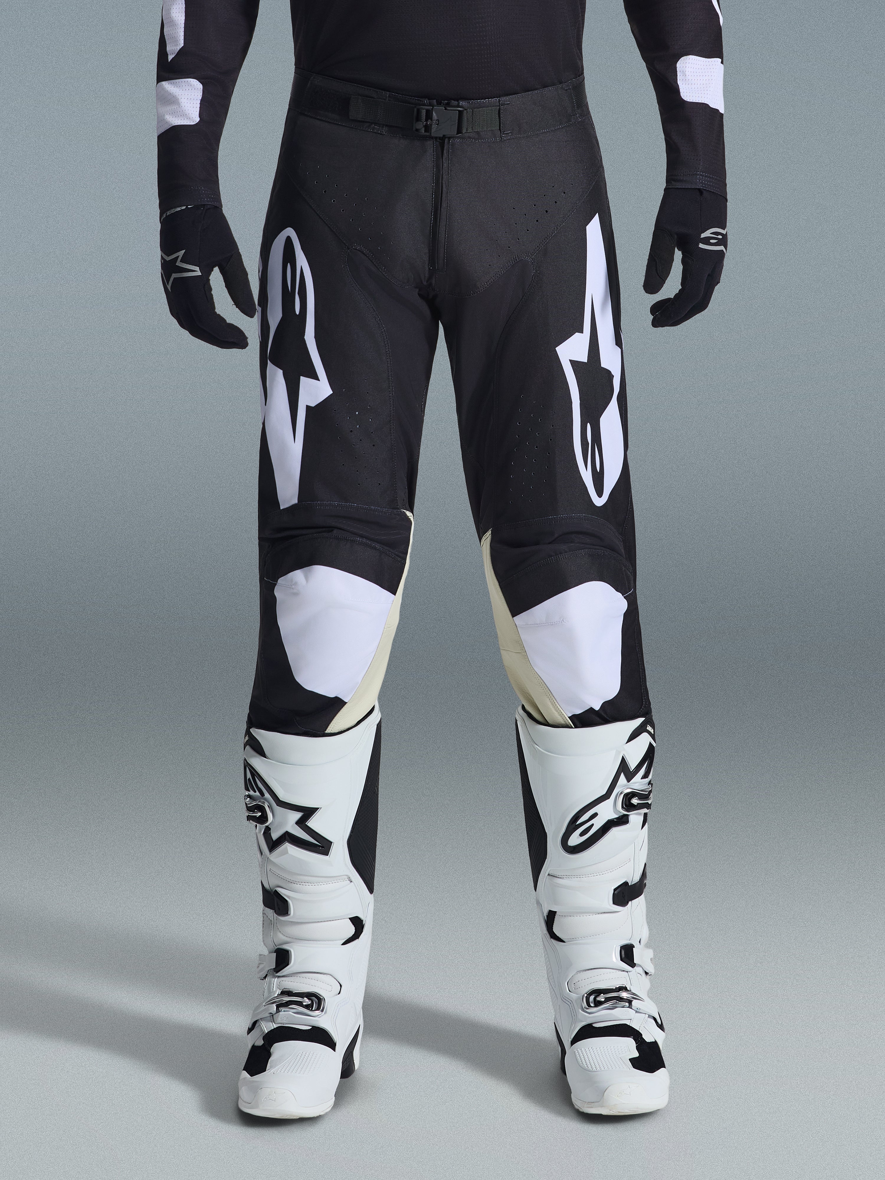 Alpinestars 2026 Racer Air Riway Pants, spodnie motocrossowe, czarno-białe, z wyraźnymi białymi logotypami Alpinestars na udach i panelach kolanowych, w zestawieniu z biało-czarnymi butami motocrossowymi i czarnymi rękawicami, sportowy krój race-fit do jazdy off-road