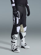 Spodnie Alpinestars Racer Air Riway 2026, spodnie motocrossowe, czarno-białe z dużą białą grafiką logo, beżowe skórzane panele na wewnętrznej stronie kolan, biało-czarne buty off-road, czarne rękawice