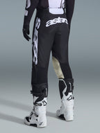 Alpinestars 2026 Racer Air Riway Pants, widok od tyłu, czarno-białe, z wyraźnym białym brandingiem „astars” na siedzeniu i nogawce, kremowe skórzane panele po wewnętrznej stronie kolan, noszone z pasującymi czarno-białymi butami i koszulką motocrossową