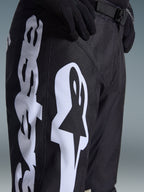 Alpinestars 2026 Racer Air Riway Pants, spodnie motocrossowe, czarno-białe, zbliżenie pokazujące duże białe logo Alpinestars, laserowo wycinane perforacje zapewniające przepływ powietrza oraz regulowaną klamrę w pasie, wytrzymały materiał do jazdy w terenie.
