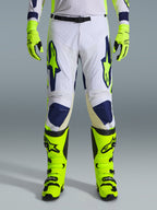 Alpinestars 2026 Racer Air Riway Pants, spodnie motocrossowe, jasnoszare, neonowożółte i niebieskie, noszone z pasującymi neonowożółtymi rękawicami i butami, z perforowanymi przednimi panelami zapewniającymi przepływ powietrza, wyraziste niebieskie i żółte logo, sportowy design do jazdy terenowej