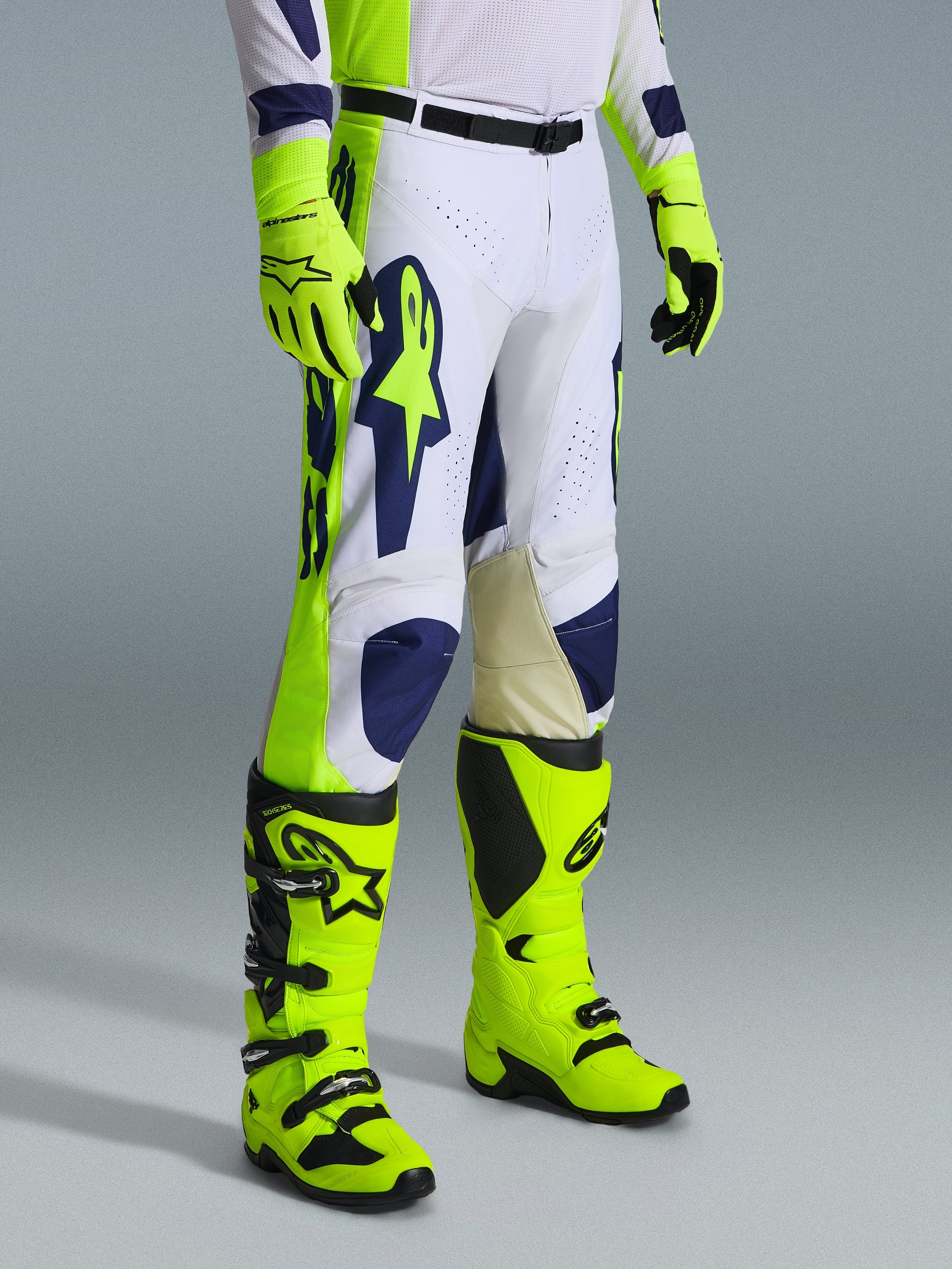 Spodnie Alpinestars 2026 Racer Air Riway, spodnie motocrossowe, jasnoszare, żółte fluo i niebieskie, noszone z dopasowanymi żółtymi fluorescencyjnymi rękawicami i butami, z dużym niebieskim logo na udzie i perforowanymi panelami wentylacyjnymi, wytrzymała odzież do motocrossu