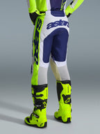 Alpinestars 2026 Racer Air Riway Pants, spodnie motocrossowe, jasnoszare, żółte fluo i niebieskie, widok z tyłu pokazujący wyraźne niebieskie logo na siedzeniu, noszone z pasującą koszulką i jaskrawożółtymi butami fluo, ergonomiczny krój race-fit