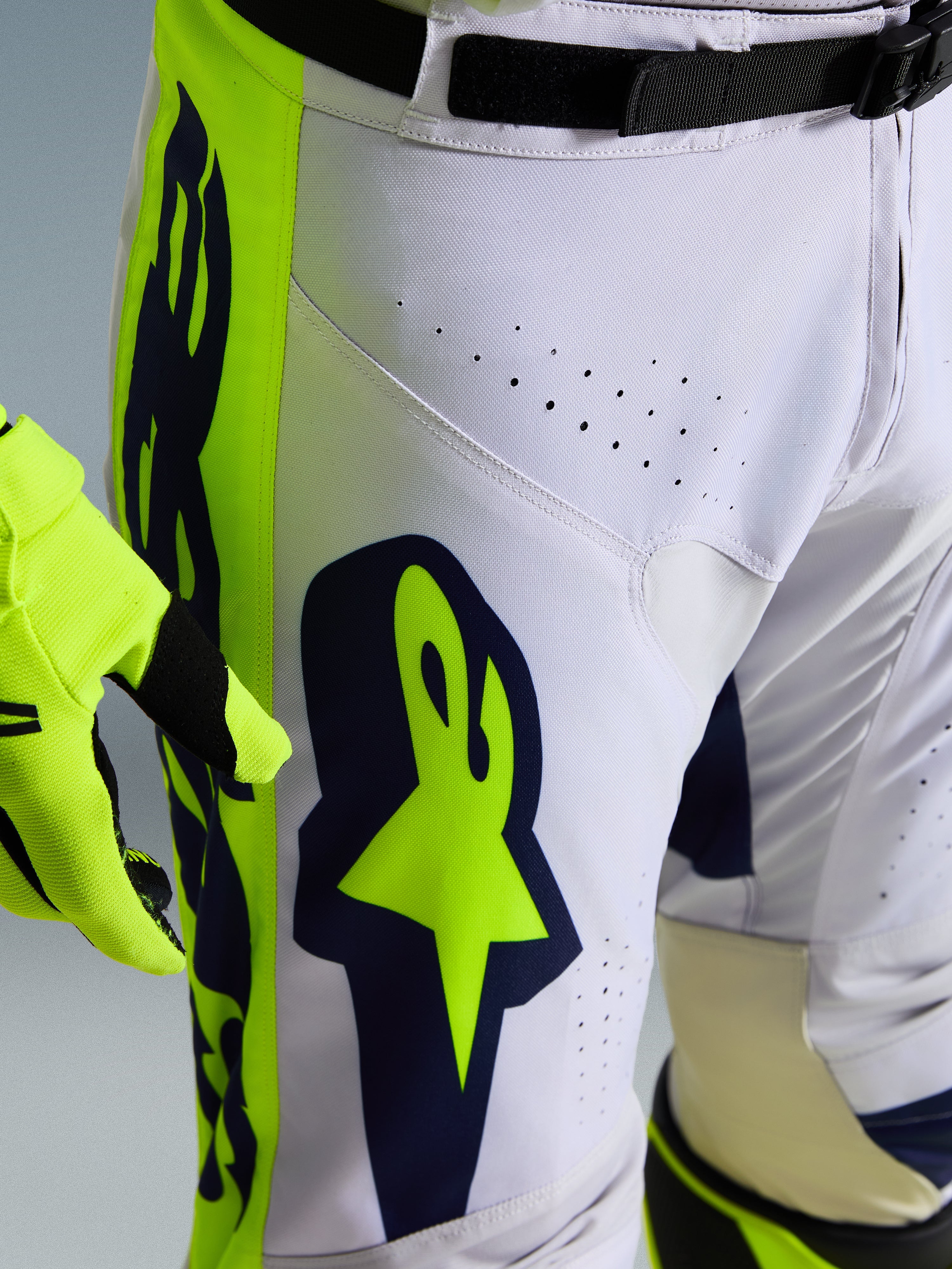 Spodnie Alpinestars 2026 Racer Air Riway, zbliżenie na biało-granatowe spodnie motocrossowe z jaskrawożółtymi panelami, laserowo wycięte otwory wentylacyjne zapewniające przepływ powietrza, wyraziste logo Astar, zestawione z pasującą żółtą rękawicą