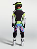 Spodnie Supertech Dyna Alpinestars, liliowo-zielona fluo odzież motocrossowa, widok z tyłu na zawodnika w stroju wyścigowym.