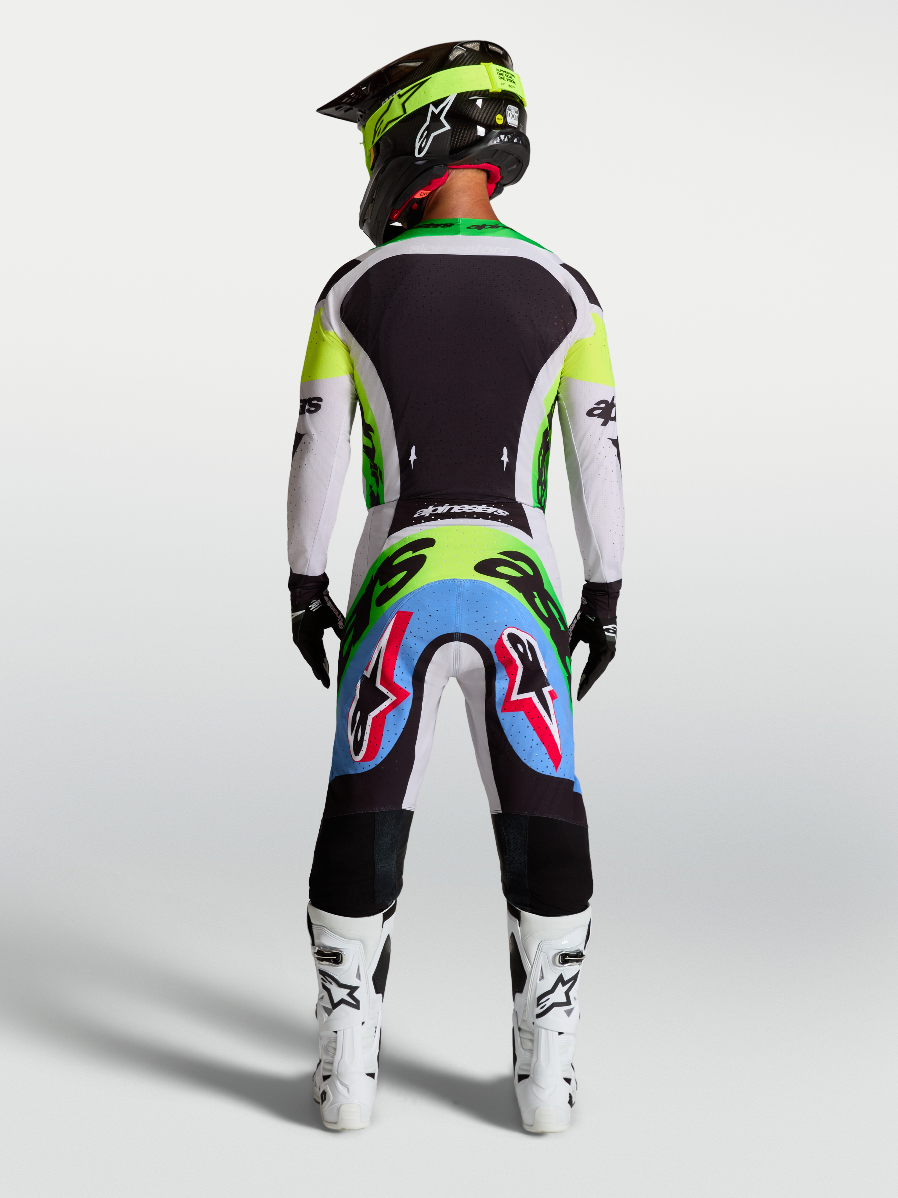 Spodnie Supertech Dyna Alpinestars, liliowo-zielona fluo odzież motocrossowa, widok z tyłu na zawodnika w stroju wyścigowym.