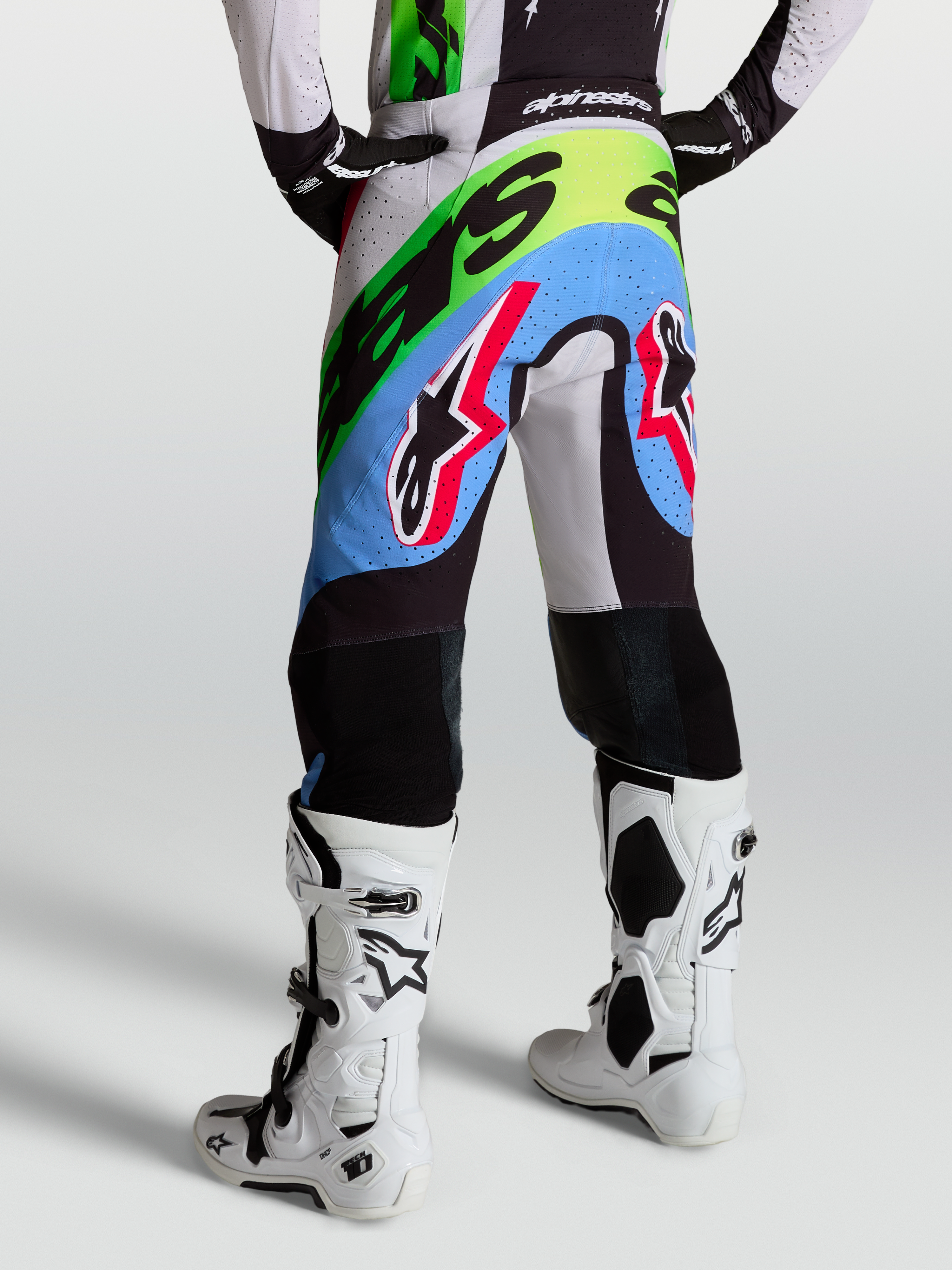 Alpinestars Spodnie Supertech Dyna, męskie spodnie motocrossowe, fioletowe, zielone i czarne, perforowana konstrukcja z kozią skórą na kolanach, pokazane od tyłu w butach Tech 10