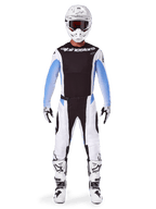 Motocrossowiec w spodniach Alpinestars 2025 Techstar Melt, spodnie motocrossowe, czarno-niebieskie, biało-czarna wielopanelowa konstrukcja z niebieskimi akcentami na biodrach, noszone z pasującą białą koszulką, białym kaskiem, białymi rękawicami i butami, kompletny zestaw do wyścigów terenowych