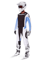 Motocyklista motocrossowy w spodniach Alpinestars 2025 Techstar Melt, biało-czarny strój motocrossowy z jasnoniebieskimi akcentami, dopasowana koszulka i rękawice, biały kask i gogle, biało-czarne buty wyścigowe, profesjonalny zestaw off-road