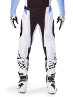 Alpinestars 2025 Techstar Melt Pants, spodnie motocrossowe, biało-czarne z jasnoniebieskimi akcentami, noszone z dopasowanymi biało-czarnymi butami i rękawicami, laserowo wycinane perforacje, wyczynowy design wyścigowy