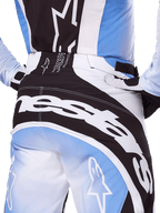 Alpinestars Techstar Melt Pants 2025, spodnie motocrossowe, czarno-biało-niebieskie, zbliżenie na tył z wyraźnym białym brandingiem na siedzeniu, zestawione z pasującą koszulką i rękawicami Techstar Melt, profesjonalna odzież wyścigowa do motocrossu