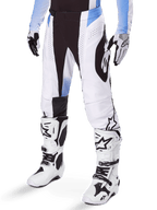 Spodnie Alpinestars Techstar Melt 2025, spodnie motocrossowe, białe i czarne z niebieskimi akcentami, laserowo wycinane perforacje dla przepływu powietrza i konstrukcja kolan Babel, noszone z dopasowanymi białymi butami i rękawicami motocrossowymi, sportowy design do wyścigów terenowych