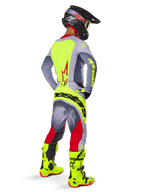 Zawodnik motocrossowy w zestawie Alpinestars 2025 Techstar Melt Gear Set, widok z tyłu, szara koszulka z neonowożółtym panelem na plecach i czerwonym logo gwiazdy, szaro-czerwone spodnie z wyraźnym neonowożółtym napisem 'Alpinestars' na siedzeniu, jaskrawe neonowożółte buty motocrossowe i pasujący kask