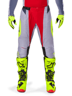 Alpinestars Techstar Melt Pants 2025, spodnie motocrossowe, kolor Bright Red Gray, szara konstrukcja z czerwonymi panelami środkowymi i neonowożółtymi akcentami, laserowo wycinane perforacje dla lepszej wentylacji, prezentowane z neonowożółtymi rękawicami i butami, profesjonalny sprzęt do wyścigów off-road