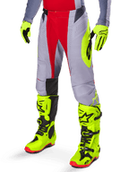 Alpinestars 2025 Techstar Melt Pants, spodnie motocrossowe, jasnoczerwone i szare, z wyrazistym neonowym żółtym logo, noszone z pasującymi neonowymi żółtymi rękawicami i butami, sportowy krój do wyścigów motocrossowych