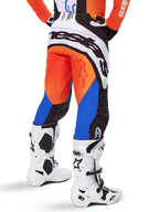 Alpinestars 2025 Techstar Melt Pants, spodnie motocrossowe, pomarańczowo-niebieskie, widok z tyłu, z dużym białym logo na siedzeniu, zestawione z pasującą pomarańczową koszulką i białymi butami Tech 10, wytrzymała odzież wyścigowa off-road