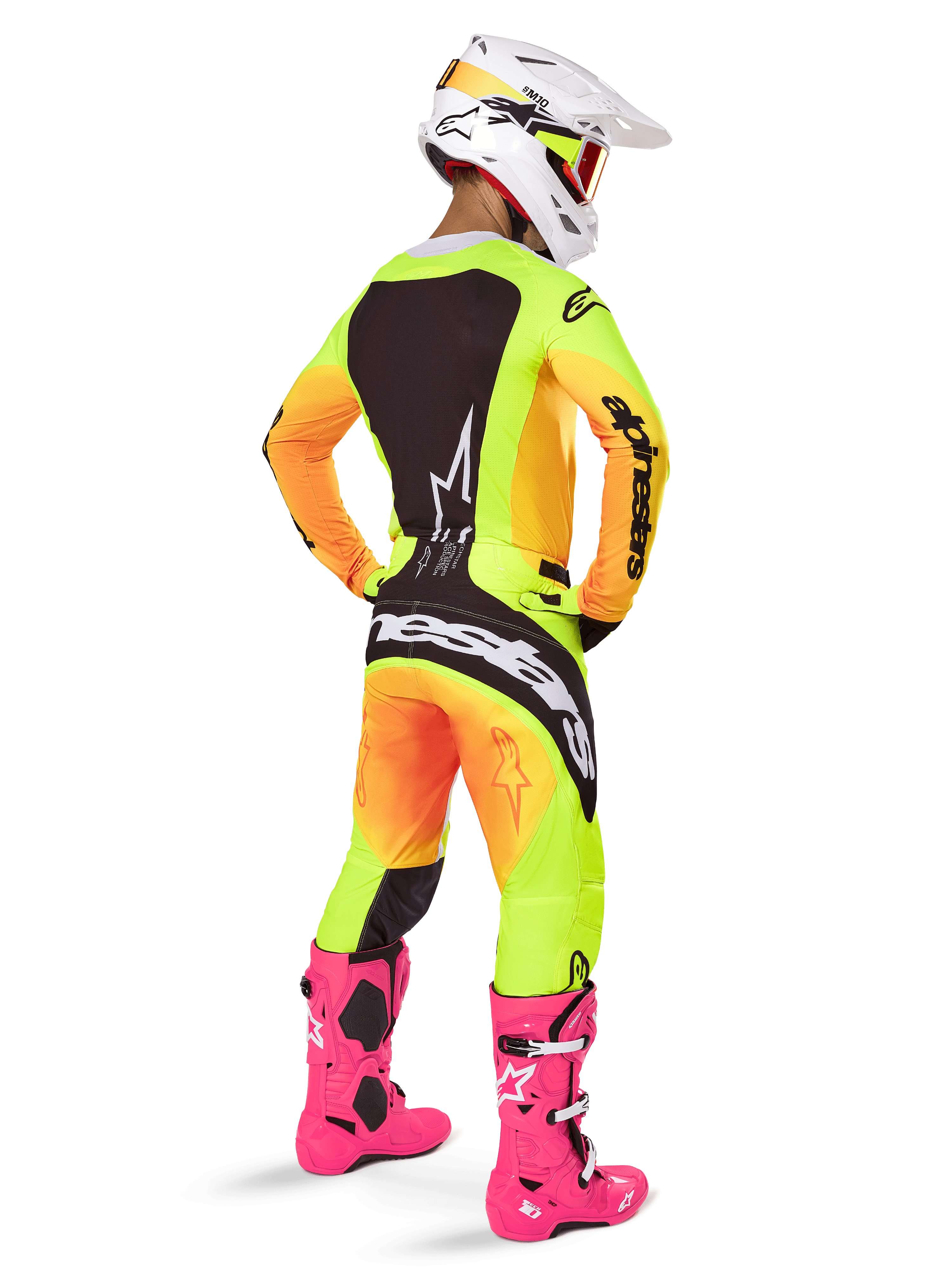 Motocyklista motocrossowy widziany od tyłu w zestawie Alpinestars 2025 Techstar Melt, żółto-pomarańczowa koszulka i spodnie z gradientem i czarnymi panelami, biały kask z czerwonymi goglami, jaskraworóżowe buty, profesjonalny strój wyścigowy do jazdy terenowej