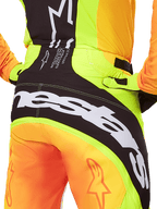 Spodnie Alpinestars Techstar Melt 2025, spodnie motocrossowe, zbliżenie na tył, neonowy żółty i pomarańczowy z czarnymi panelami, duże białe logo Alpinestars na siedzeniu, profesjonalna odzież do jazdy terenowej