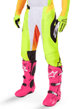 Spodnie Alpinestars Techstar Melt 2025, spodnie motocrossowe, neonowożółte z białymi i pomarańczowymi akcentami, czarne wzory po bokach, noszone z jaskraworóżowymi butami motocrossowymi i neonowożółtymi rękawicami, z perforowaną wentylacją, wytrzymały terenowy sprzęt wyścigowy