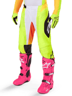 Spodnie Alpinestars Techstar Melt 2025, spodnie motocrossowe, neonowożółte z białymi i pomarańczowymi akcentami, czarne wzory po bokach, noszone z jaskraworóżowymi butami motocrossowymi i neonowożółtymi rękawicami, z perforowaną wentylacją, wytrzymały terenowy sprzęt wyścigowy
