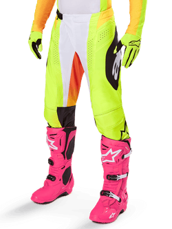 Spodnie Alpinestars Techstar Melt 2025, spodnie motocrossowe, neonowożółte z białymi i pomarańczowymi akcentami, czarne wzory po bokach, noszone z jaskraworóżowymi butami motocrossowymi i neonowożółtymi rękawicami, z perforowaną wentylacją, wytrzymały terenowy sprzęt wyścigowy