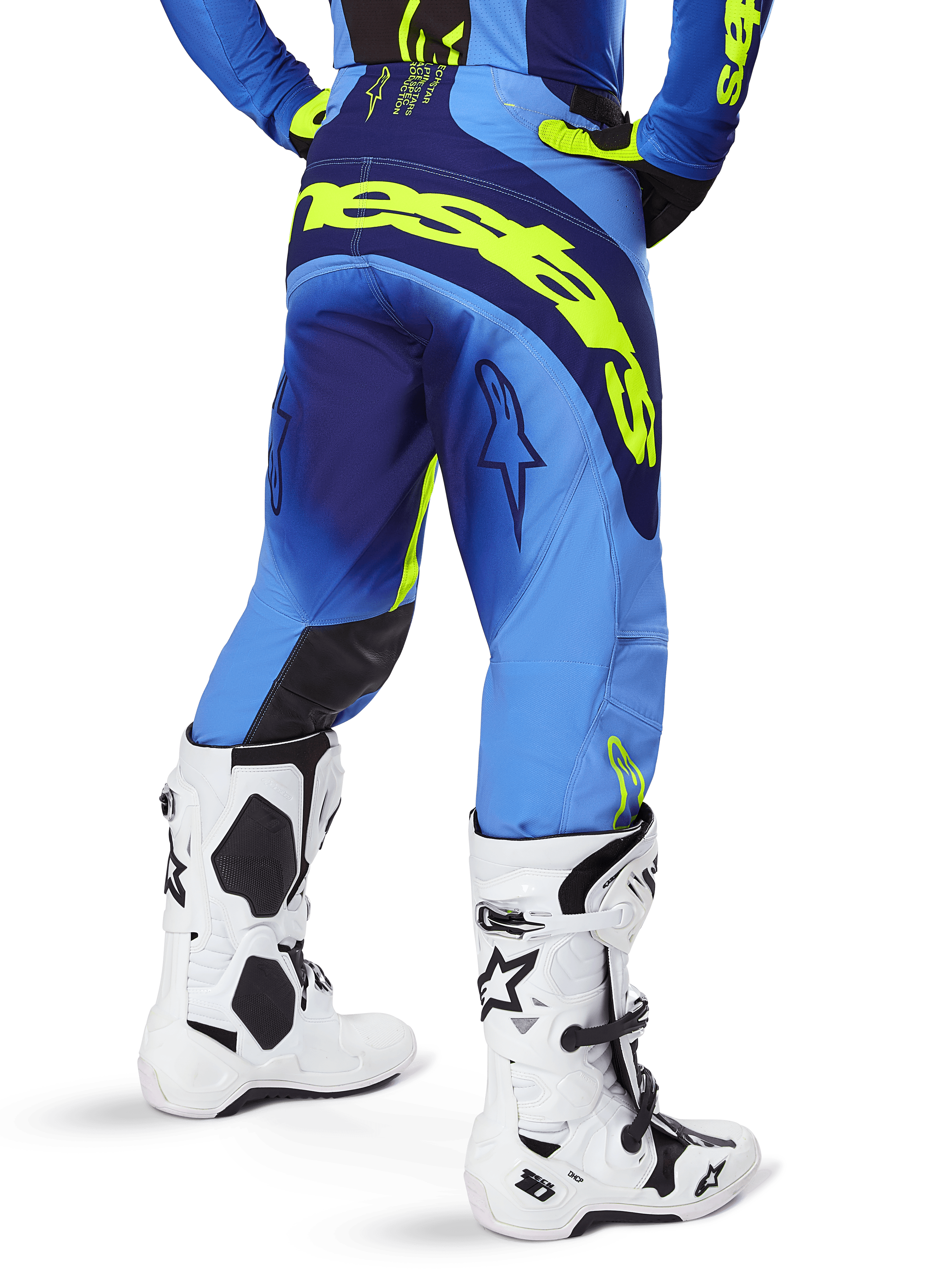 Alpinestars Techstar Melt Pants 2025, spodnie motocrossowe, niebieskie i żółte fluo, widok z tyłu przedstawiający duże żółte logo na siedzeniu i udach, noszone z białymi butami motocrossowymi i dopasowaną niebieską koszulką, sportowy krój wyścigowy do jazdy w terenie